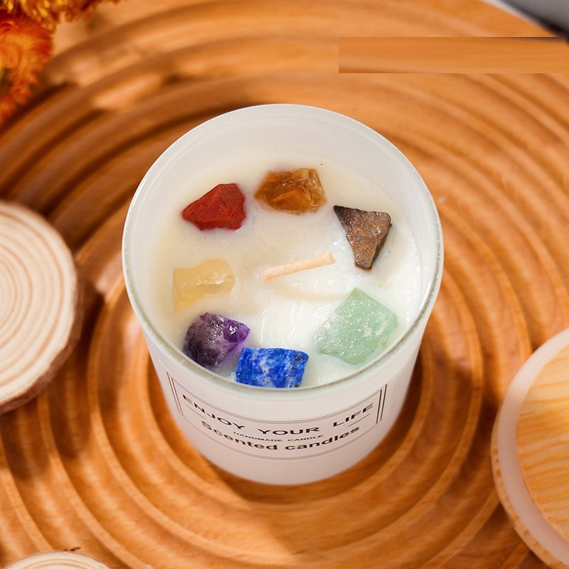 Candle with colorful stones in a white container on a wooden surface
